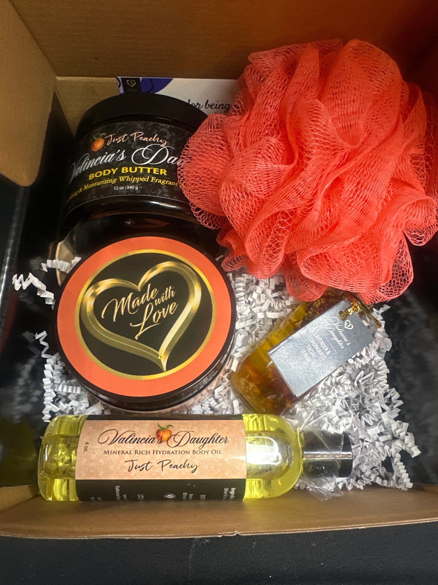 The gift box contains 12 oz. body butter, 12 oz. body scrub, 4 oz. body oil, 2oz. vitamin E & C infused facial serum, small wooden spoon & loofah