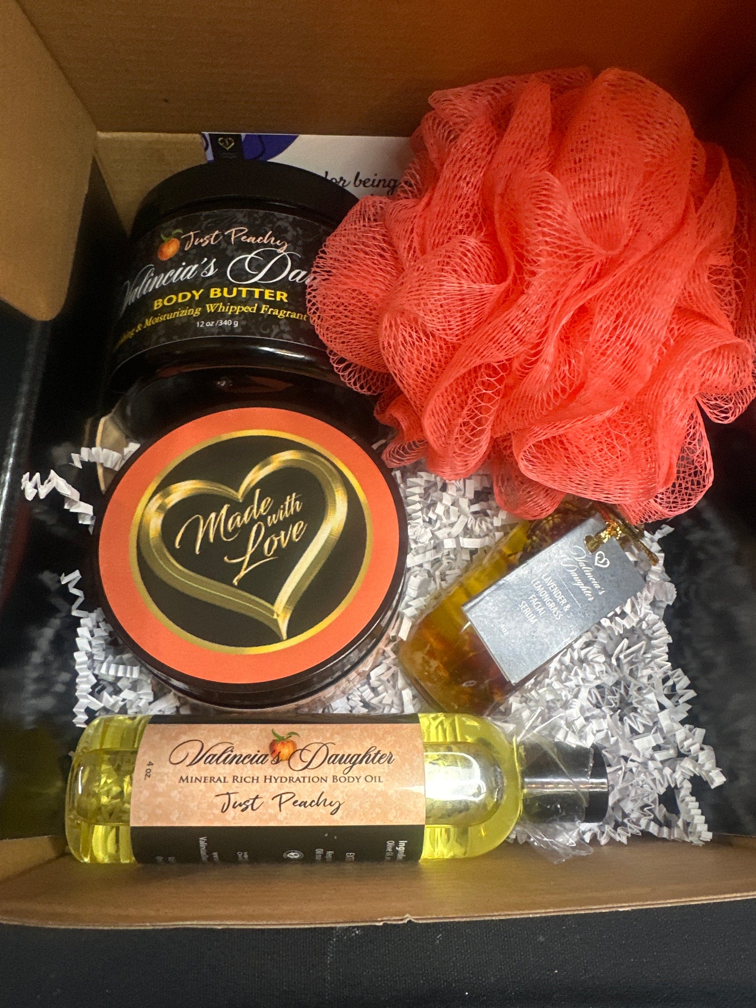 The gift box contains 12 oz. body butter, 12 oz. body scrub, 4 oz. body oil, 2oz. vitamin E & C infused facial serum, small wooden spoon & loofah